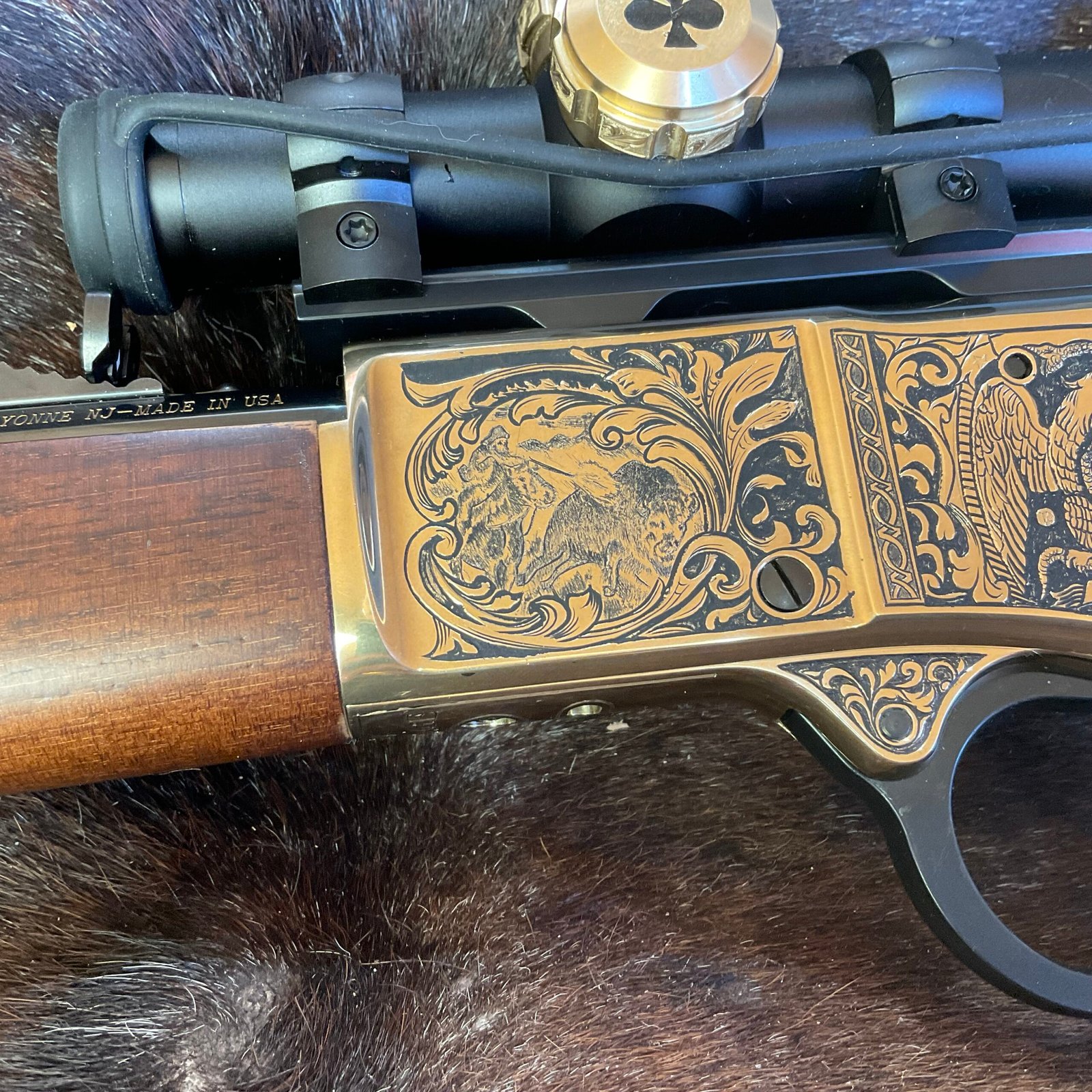 Close view of engraved gold firearm receiver with animal scene and scroll detail