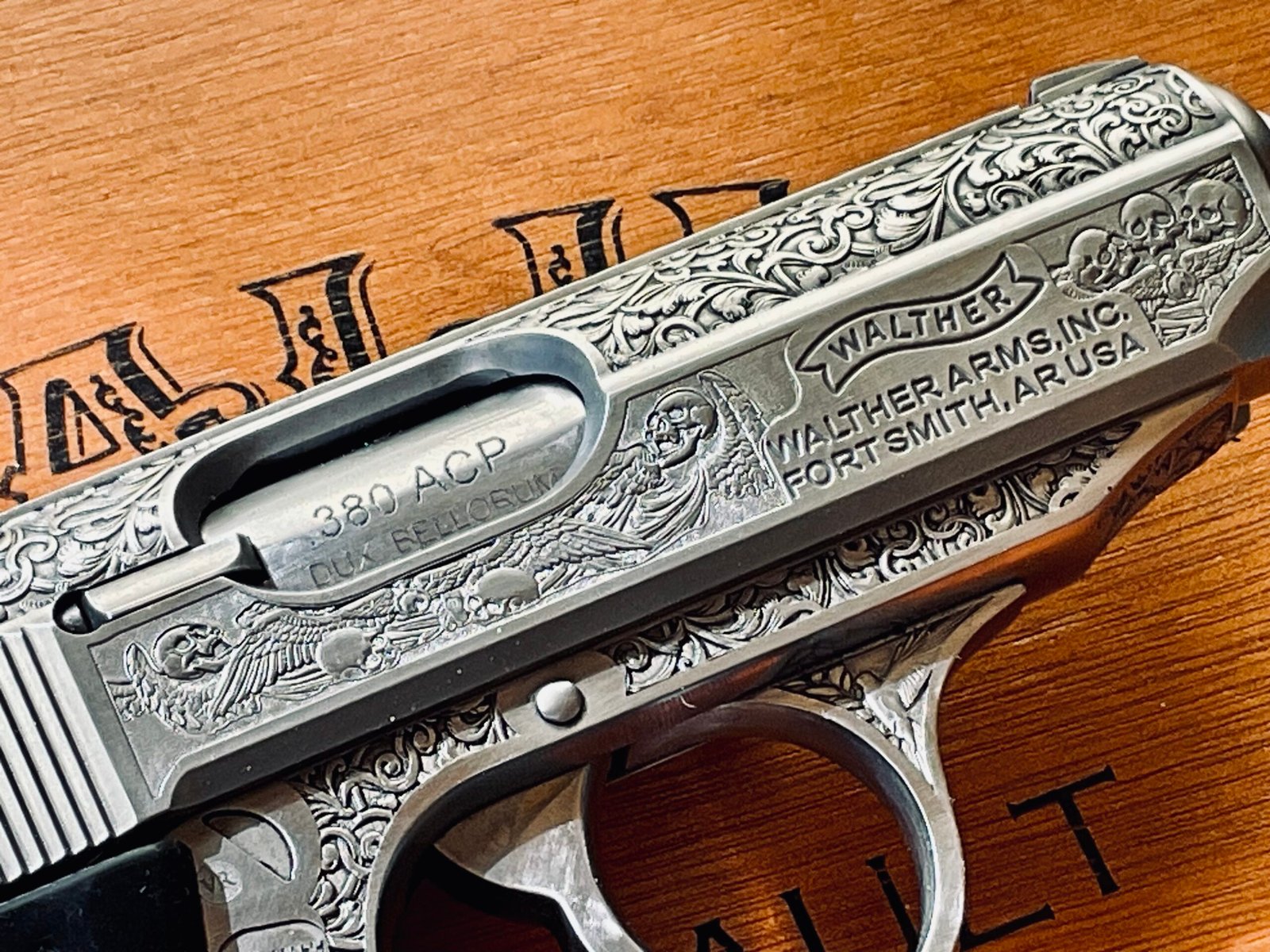 Detailed hand engraving on a stainless firearm slide with scrollwork and skull artwork